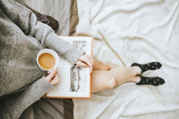 Bild zeigt Frau mit Tee Tasse und Buch in der Hand. 